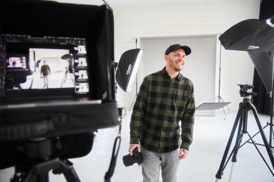 Fotograf Arne Claußen im Fotostudio mit Kamera in der Hand, umgeben von Beleuchtungsequipment und einem Stativ.