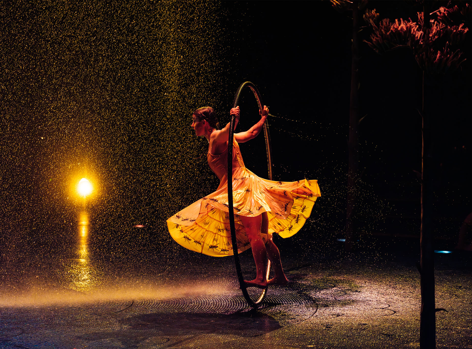 Akrobatin in gelbem Kleid bei einer Aufführung von Cirque du Soleil, umgeben von einem Wasserfall.