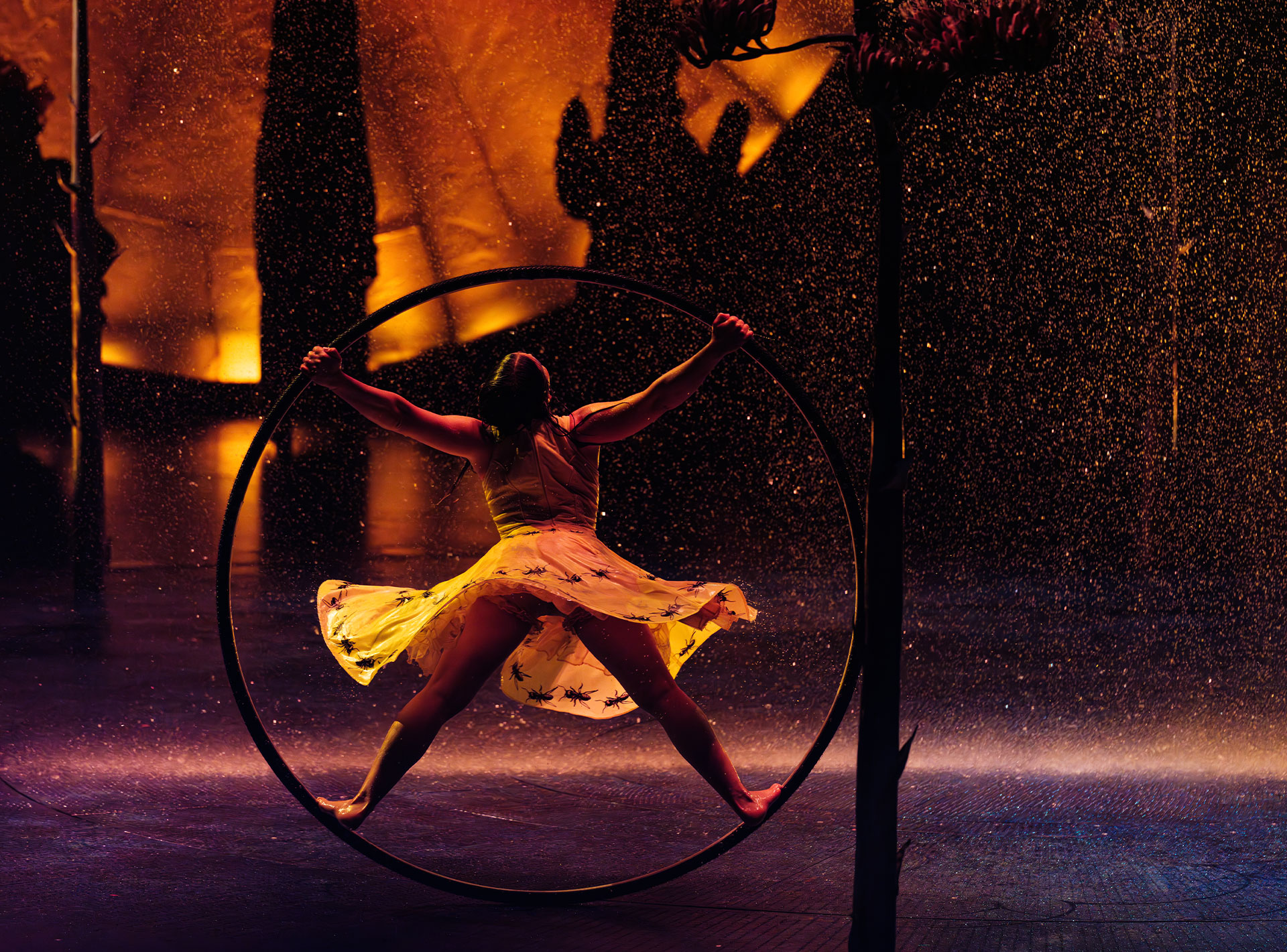 Akrobatin in einem gelben Kleid, die in einem großen Reifen unter sprühendem Wasser auftritt.