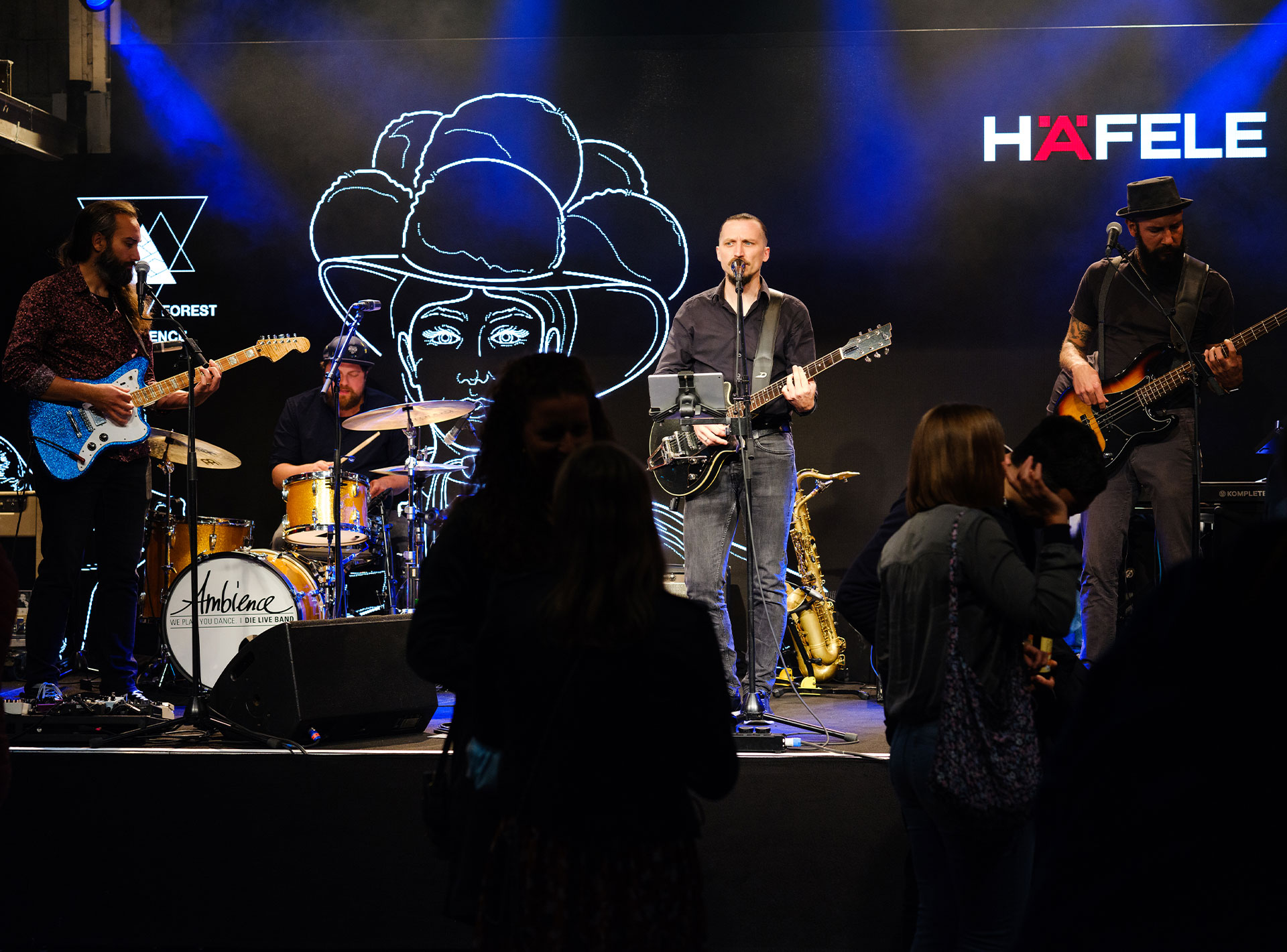 Live-Band bei einem Event mit Bühnenbeleuchtung und LED-Hintergründen, links das Logo und der Name HÄFELE.