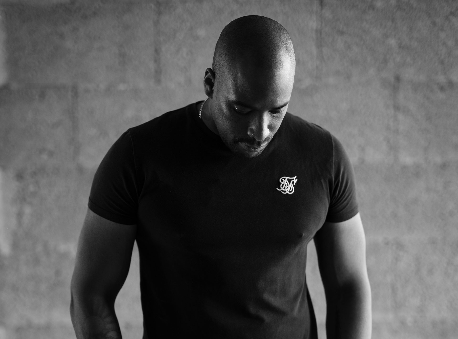 Schwarz-weiß Foto eines muskulösen Mannes in einem engen T-Shirt, der nach unten schaut.