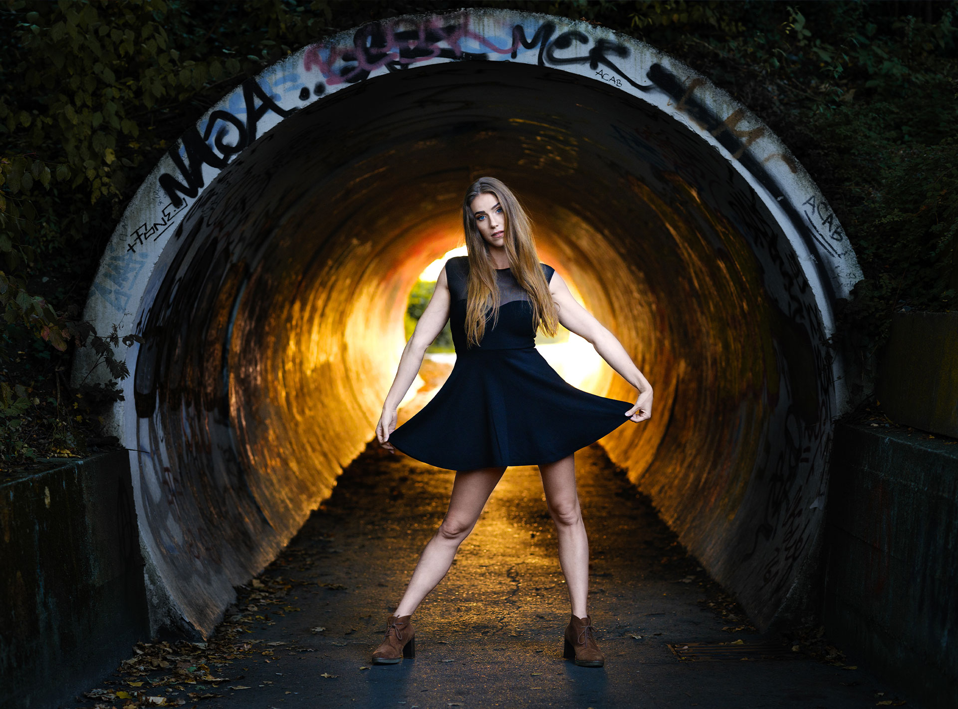 Lea Toran Jenner in einem schwarzen Kleid posiert in einem Tunnel mit Graffiti.