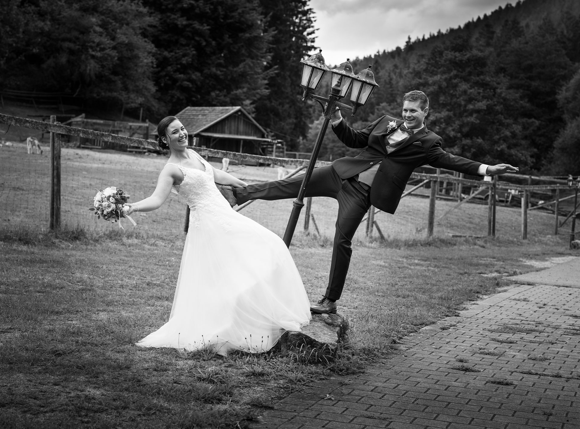 Braut und Bräutigam in einem spielerischen Moment, bei dem der Bräutigam an einer Laterne hängt und die Braut seine Hand hält.