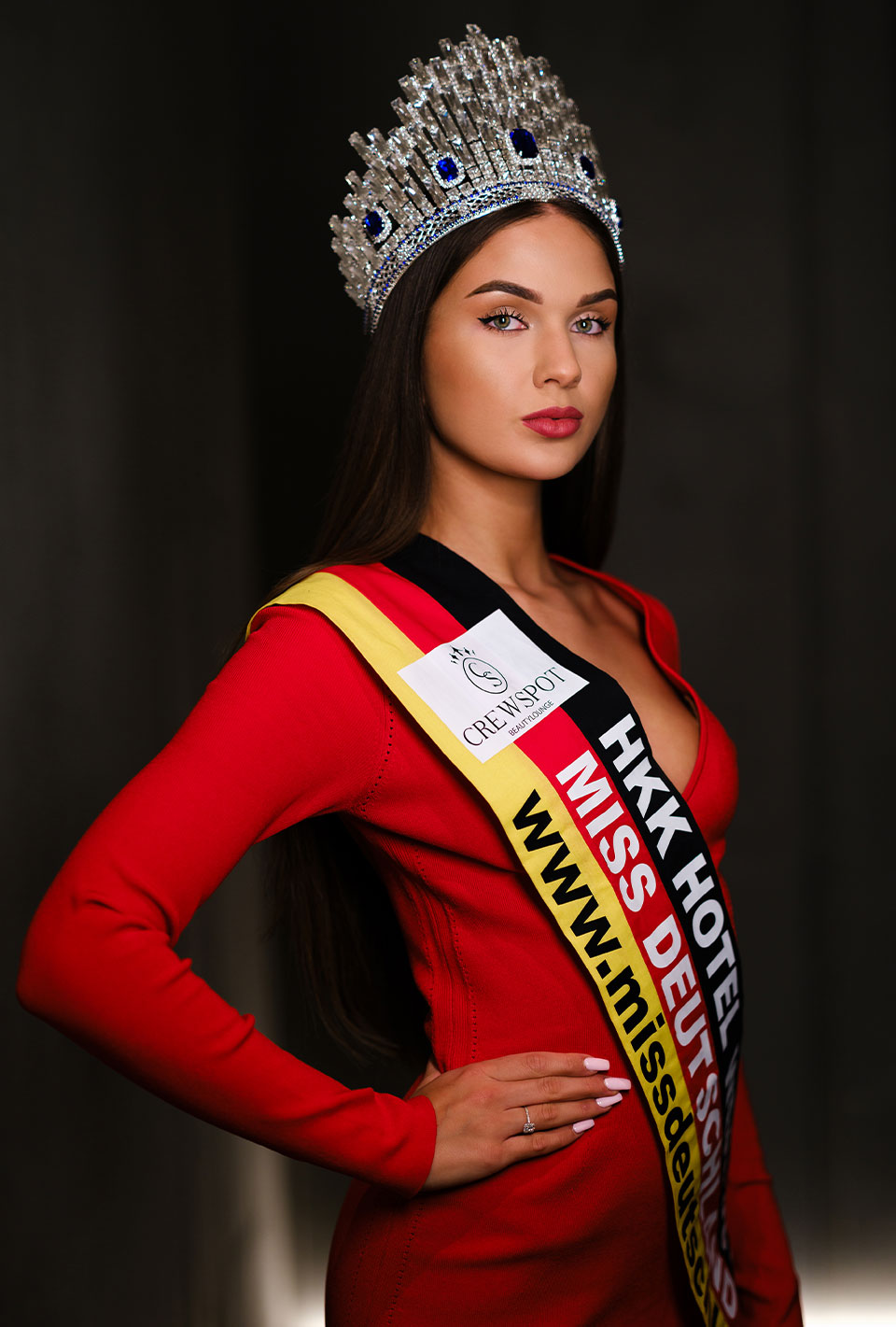 Miss Deutschland 2024 Celina Weil mit langem, dunklem Haar trägt ein rotes Kleid, eine Krone und eine Schärpe mit der Aufschrift 