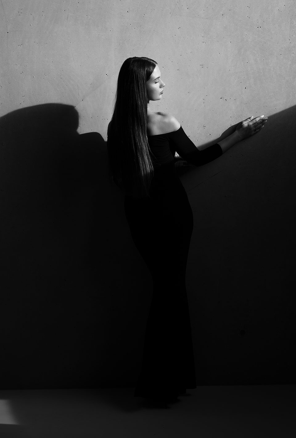 Miss Deutschland 2024 Celina Weil in einem eleganten, schulterfreien, bodenlangen schwarzen Kleid steht vor einer Betonwand.