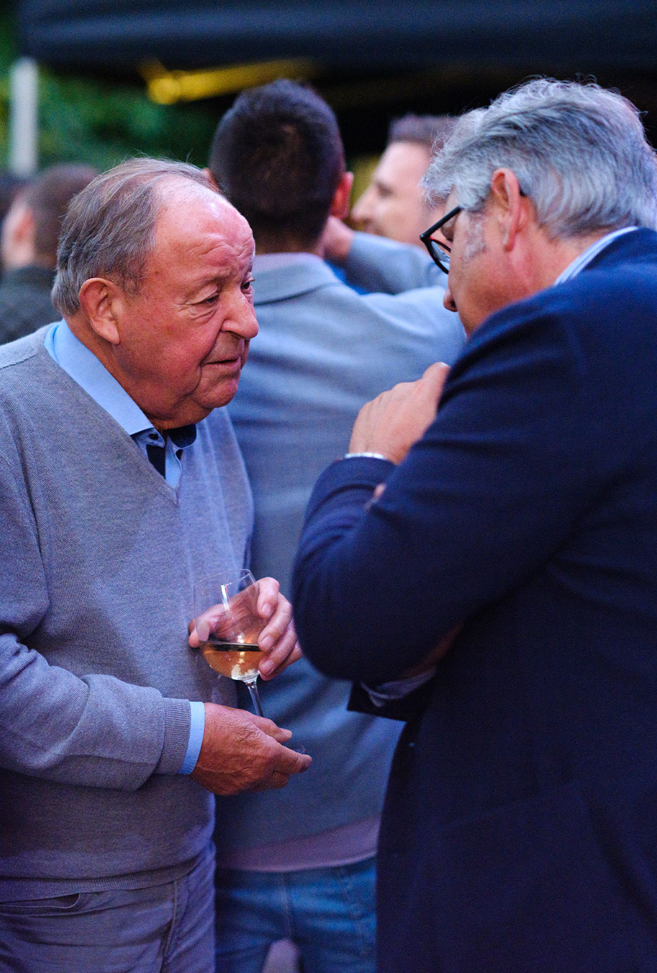 Zwei ältere Männer in Anzügen unterhalten sich bei einer Veranstaltung im Freien.
