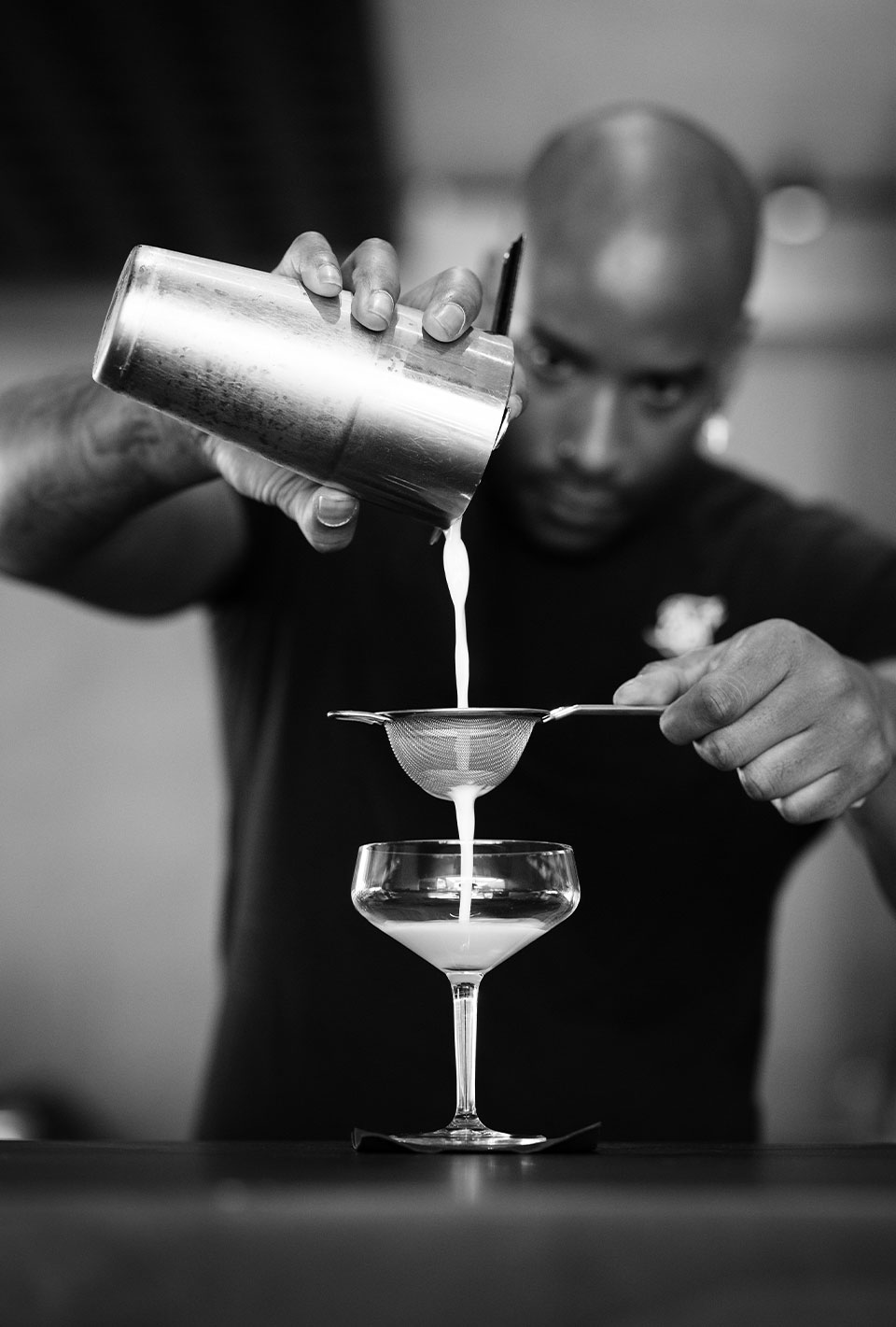 Barkeeper gießt einen weißen Cocktail durch ein Sieb in ein Glas.