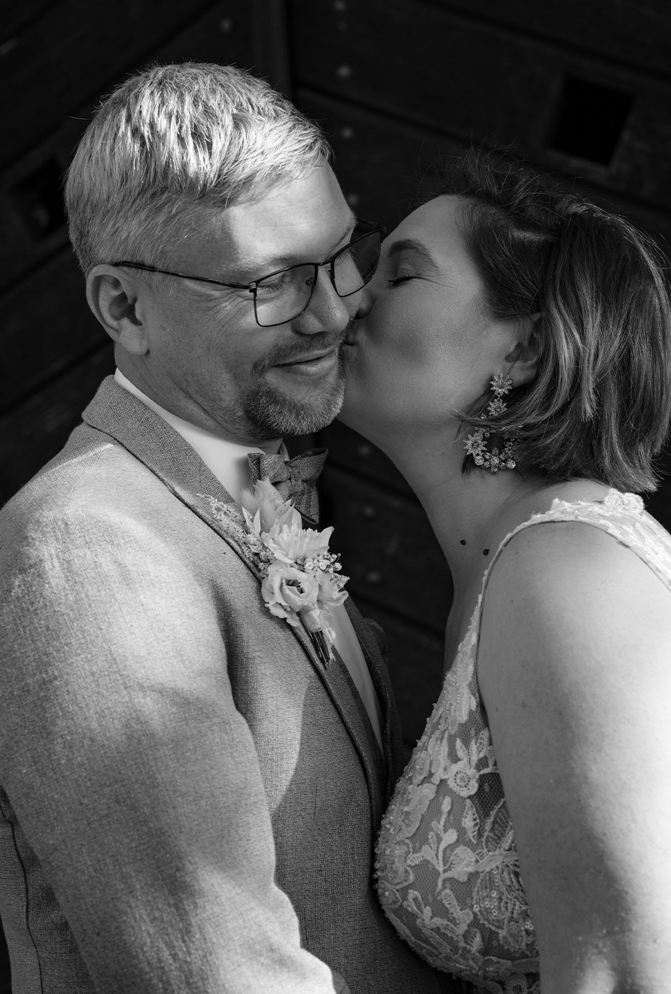 Schwarz-Weiß-Foto eines Brautpaares; die Braut küsst den Bräutigam liebevoll auf die Wange.