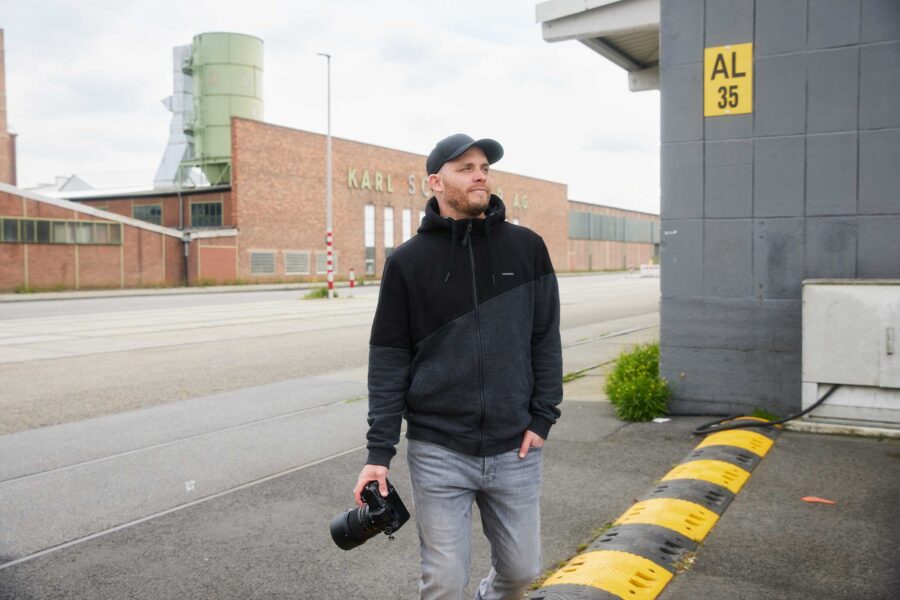 Arne Claußen in schwarzem Kapuzenpullover und Baseballmütze hält eine Kamera in der Hand.