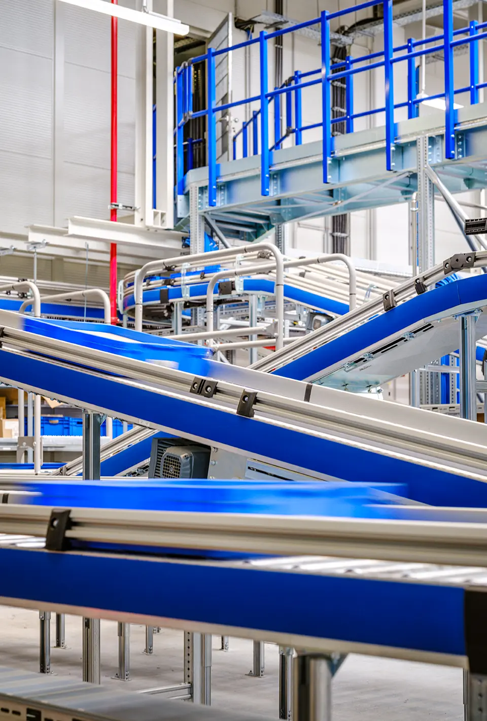 Mehrere schräg verlaufende Transportbänder in Blau und Silber in einer Produktionsanlage, helle Innenhalle mit Technikkomponenten.